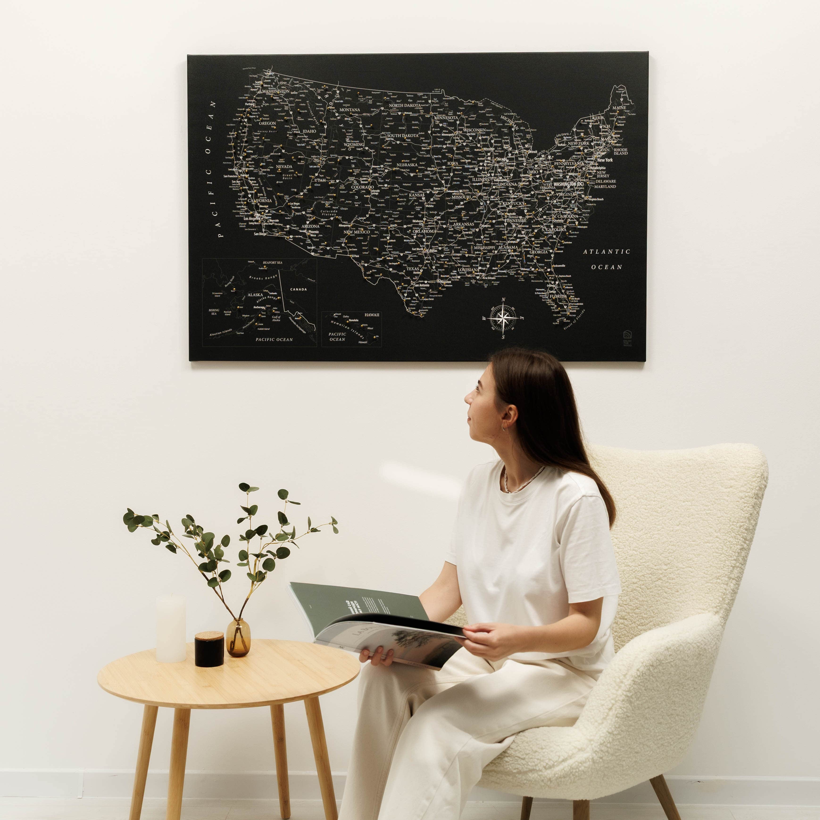 Woman sitting in a chair reading a magazine in a room with a large map of the United States on the wall.