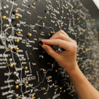 Hand placing a gold pin on a map of the United States with cities labeled.