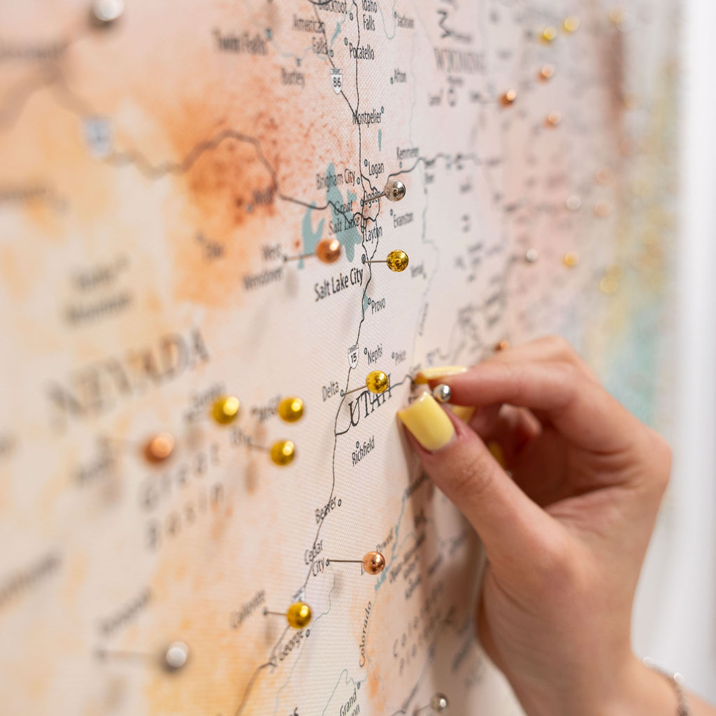 Hand with yellow nail polish pinning a gold pin to a map of Utah.