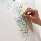 Hand with yellow nail polish pinning a gold pushpin on a map of Florida.