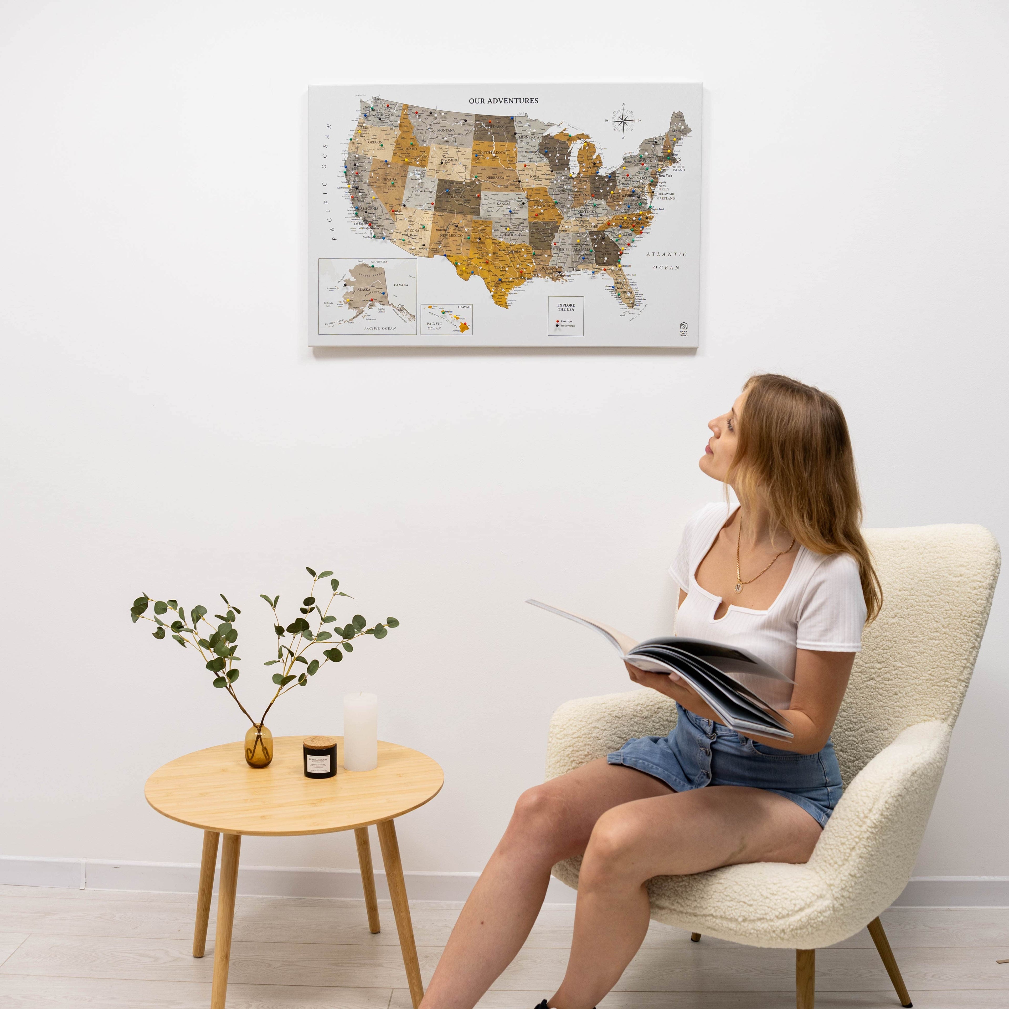 Woman sitting in a chair reading a book with a map of the United States on the wall behind her.