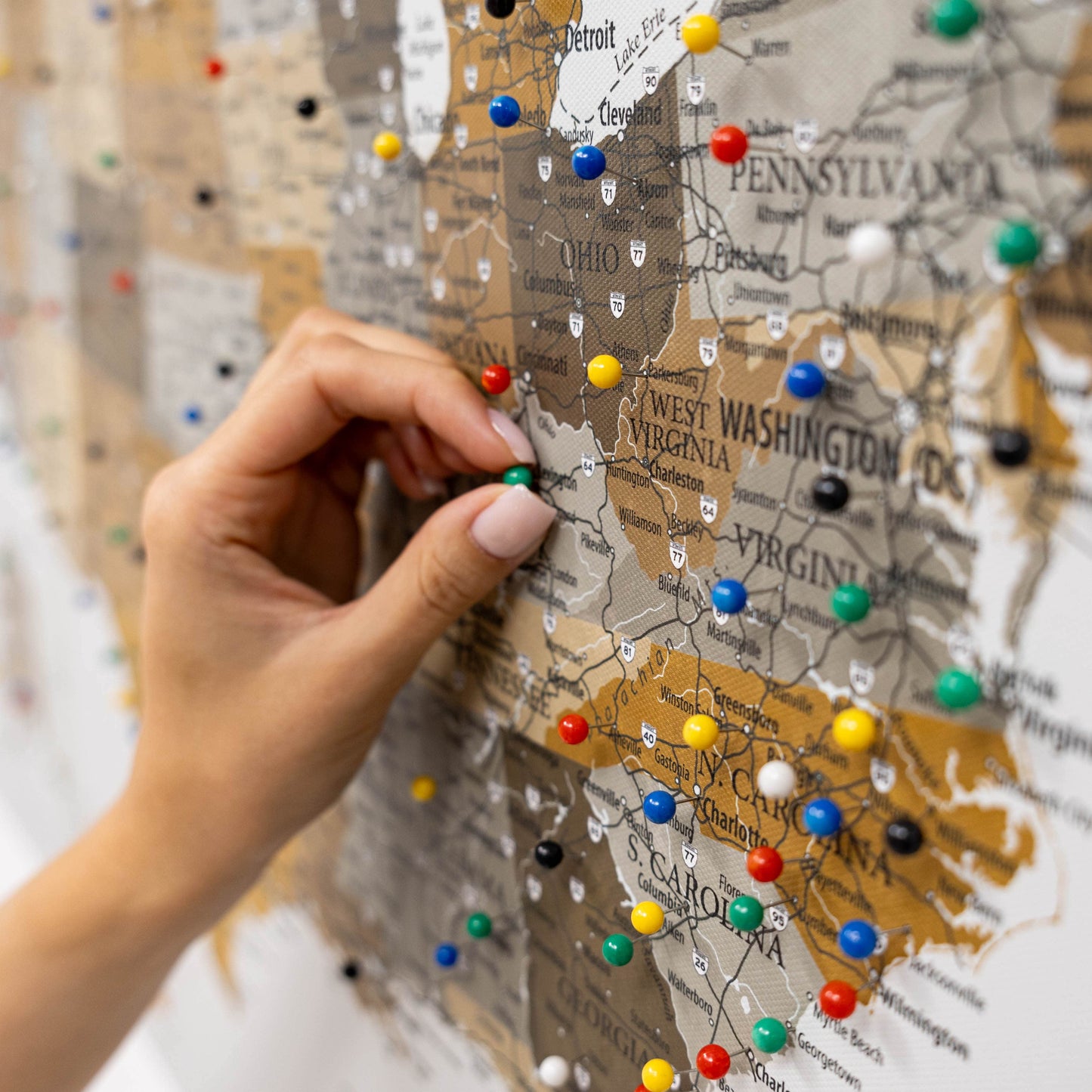 Hand placing a colorful pin on a map of the United States.