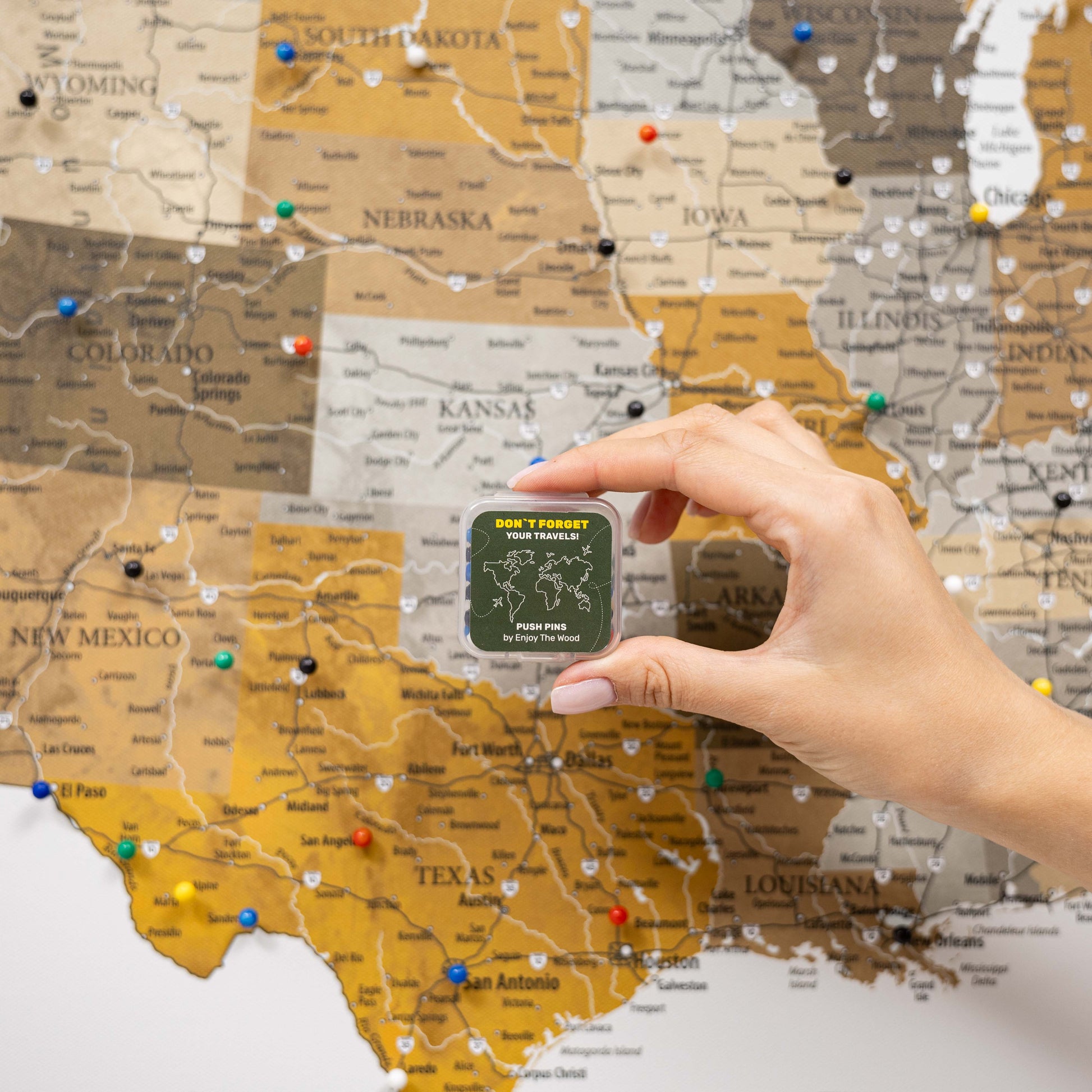 Hand placing a small green card on a map of the United States with pins.