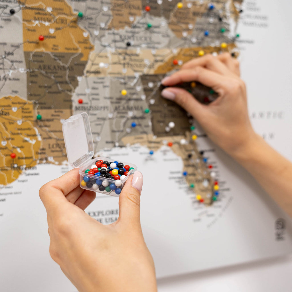 Person holding a container of colorful pins over a map