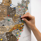 Map of the United States with colorful pins, hand placing a pin on the map.