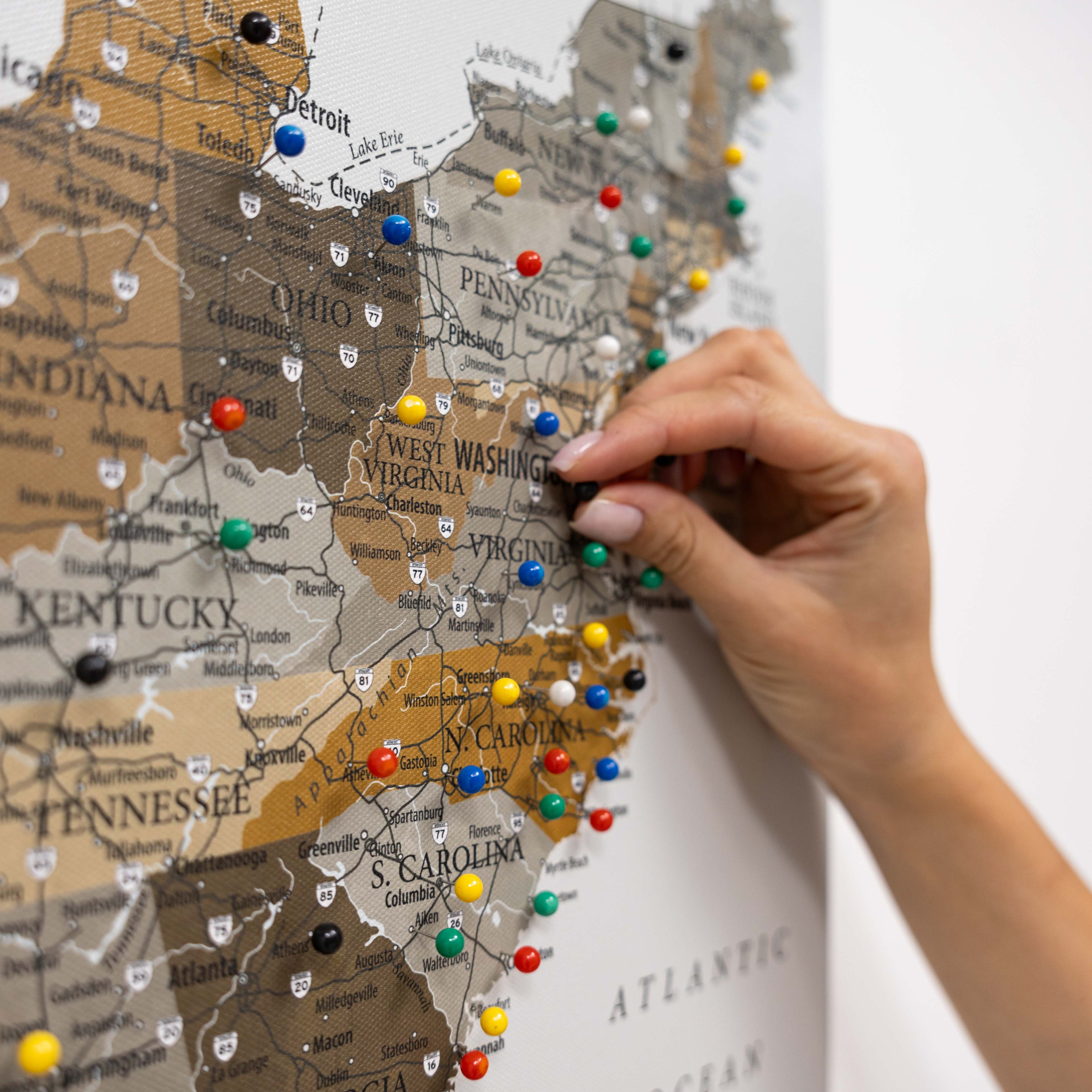 Map of the United States with colorful pins, hand placing a pin on the map.