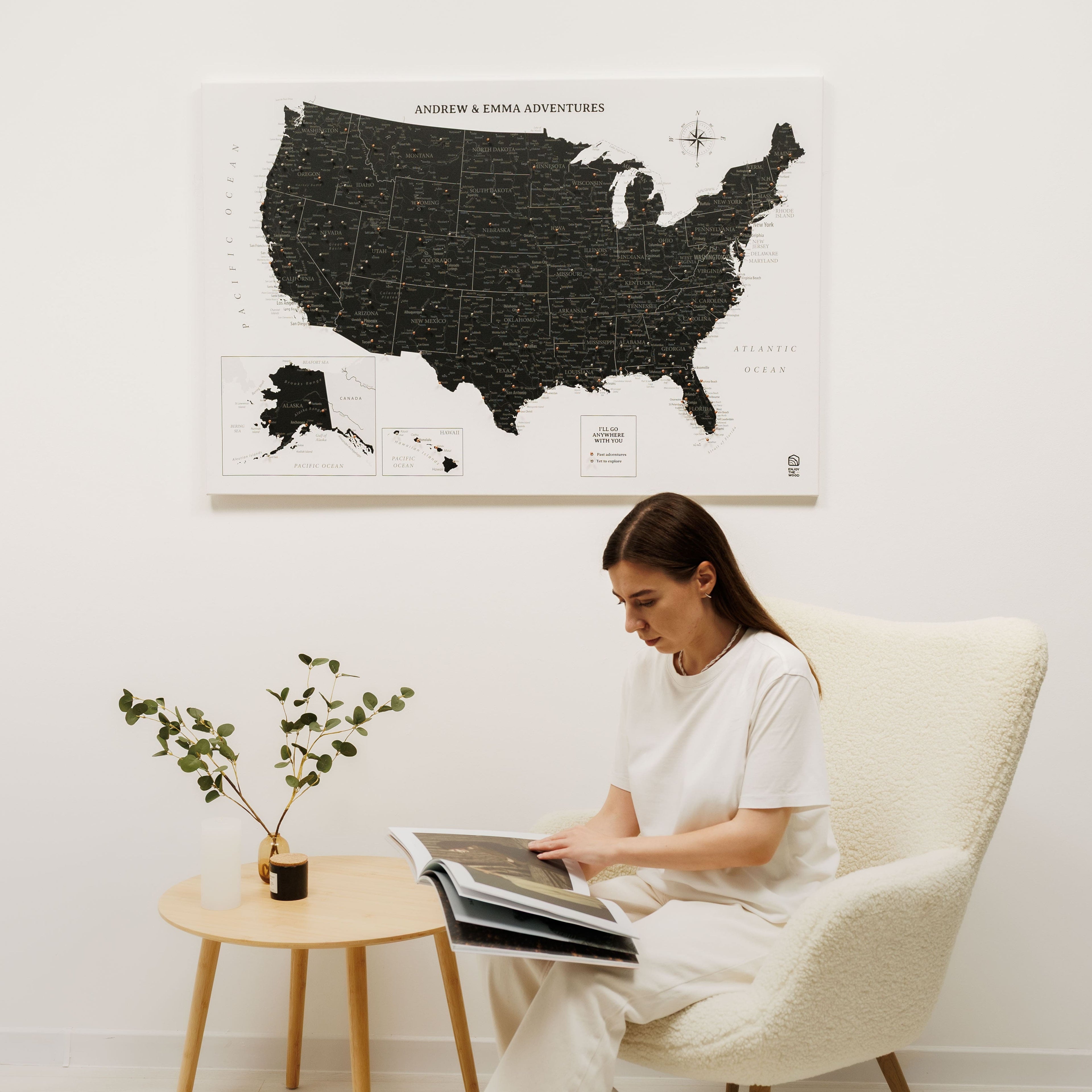 Woman sitting in a chair reading a book with a large map of the United States on the wall behind her.
