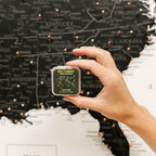 Hand holding a small green container with a world map design in front of a world map wall decoration.