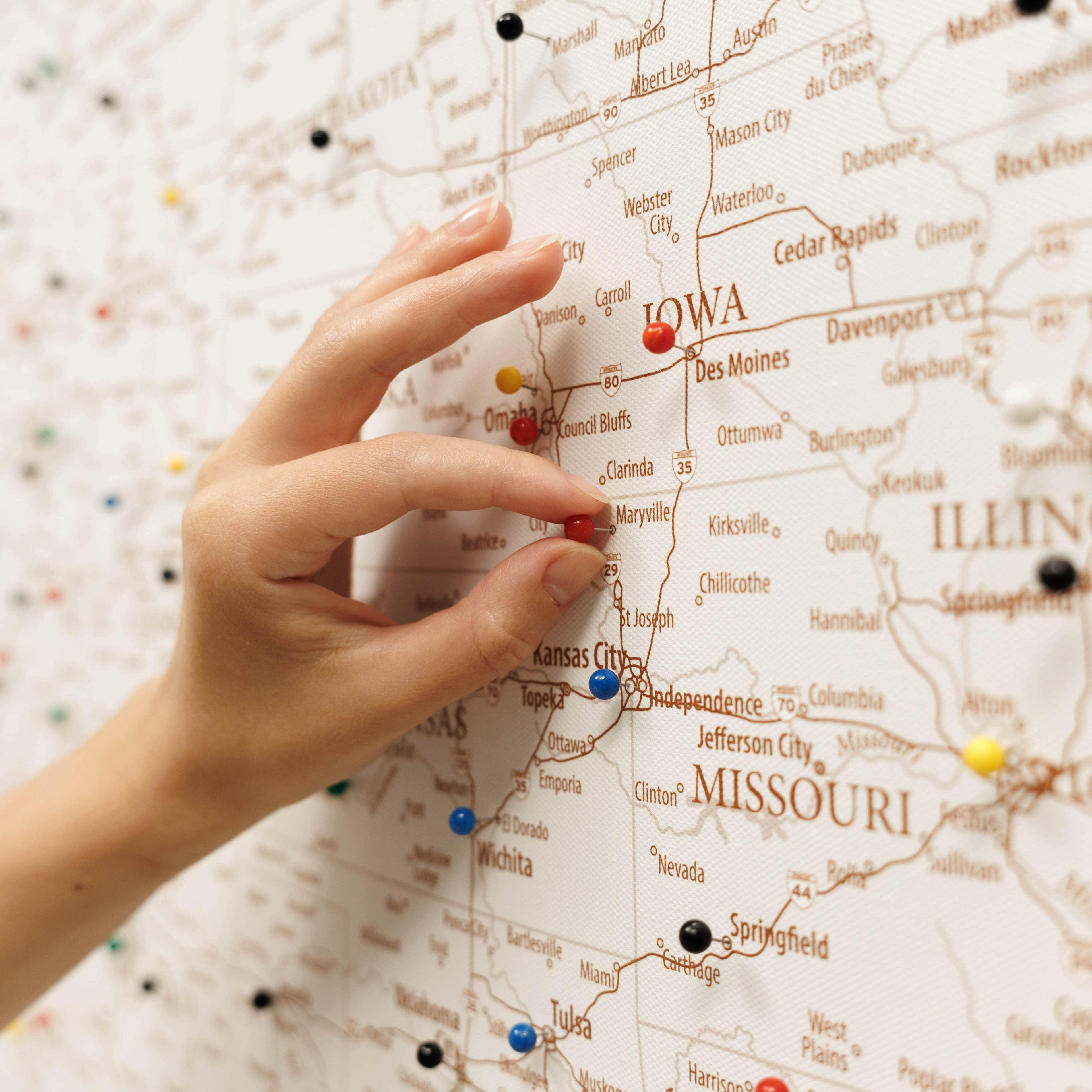 Hand placing a red pin on a map of the United States, focusing on Iowa and Missouri.