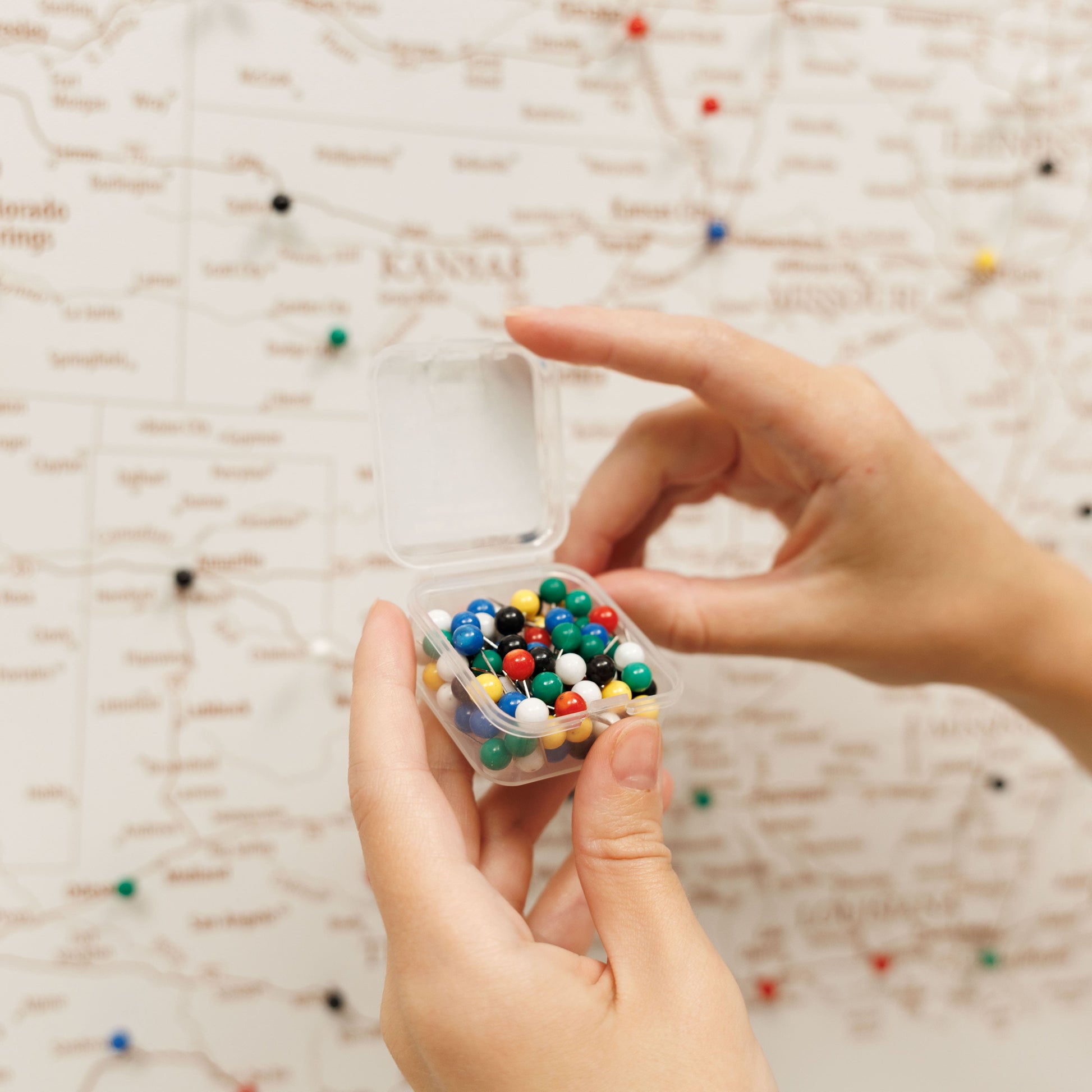 Hand holding a small transparent container filled with multicolored beads against a textured beige background.