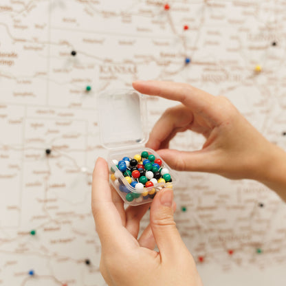 Hand holding a small transparent container filled with multicolored beads against a textured beige background.