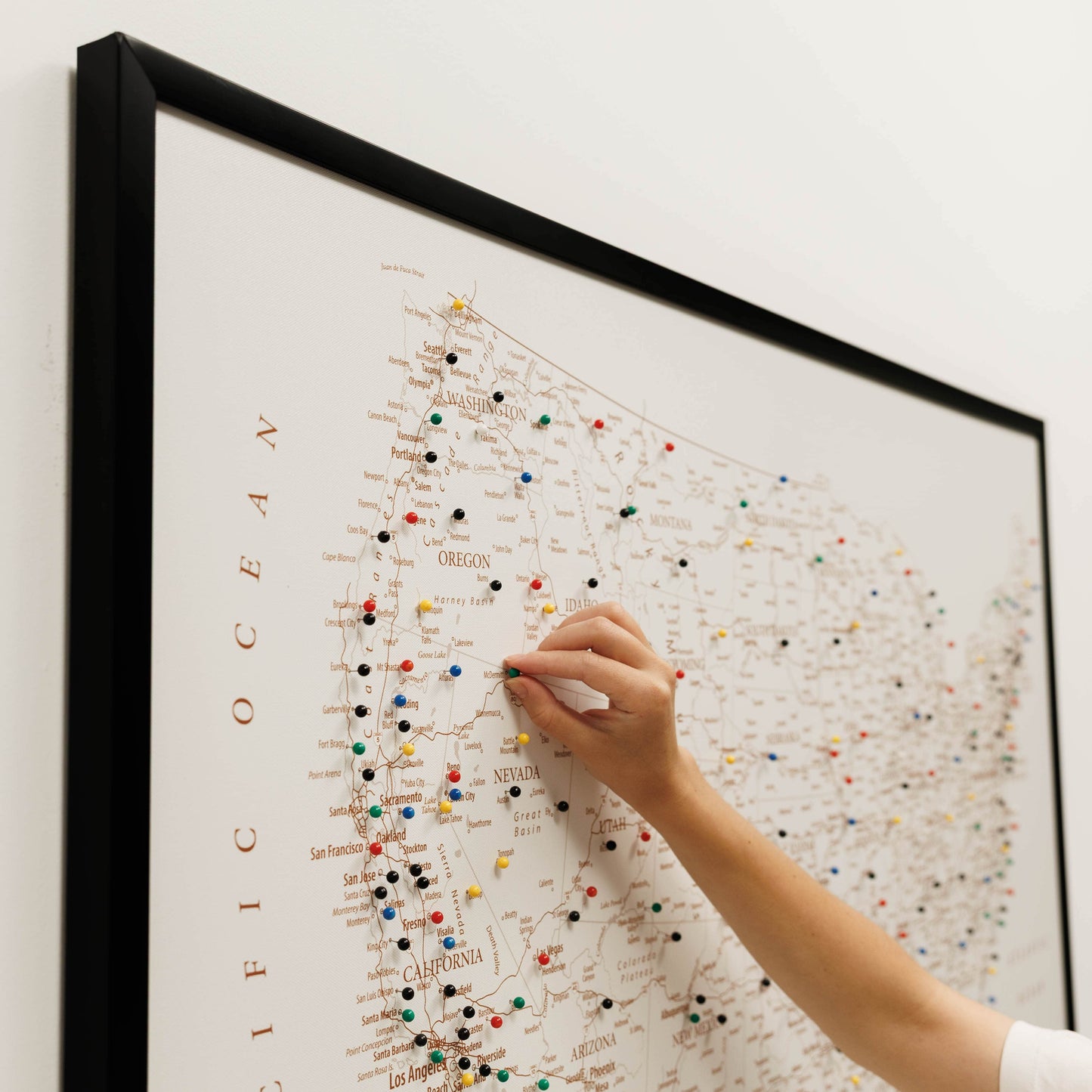 Person pinning a colorful pushpin on a framed map of the United States.