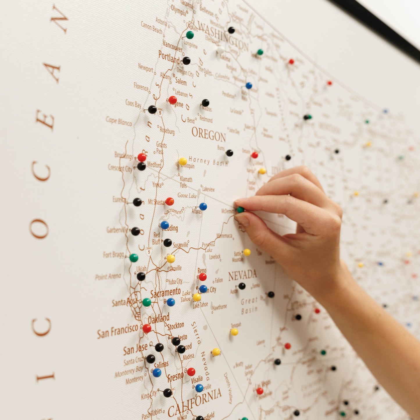 Hand placing a colorful pin on a map of California with other pins already in place.