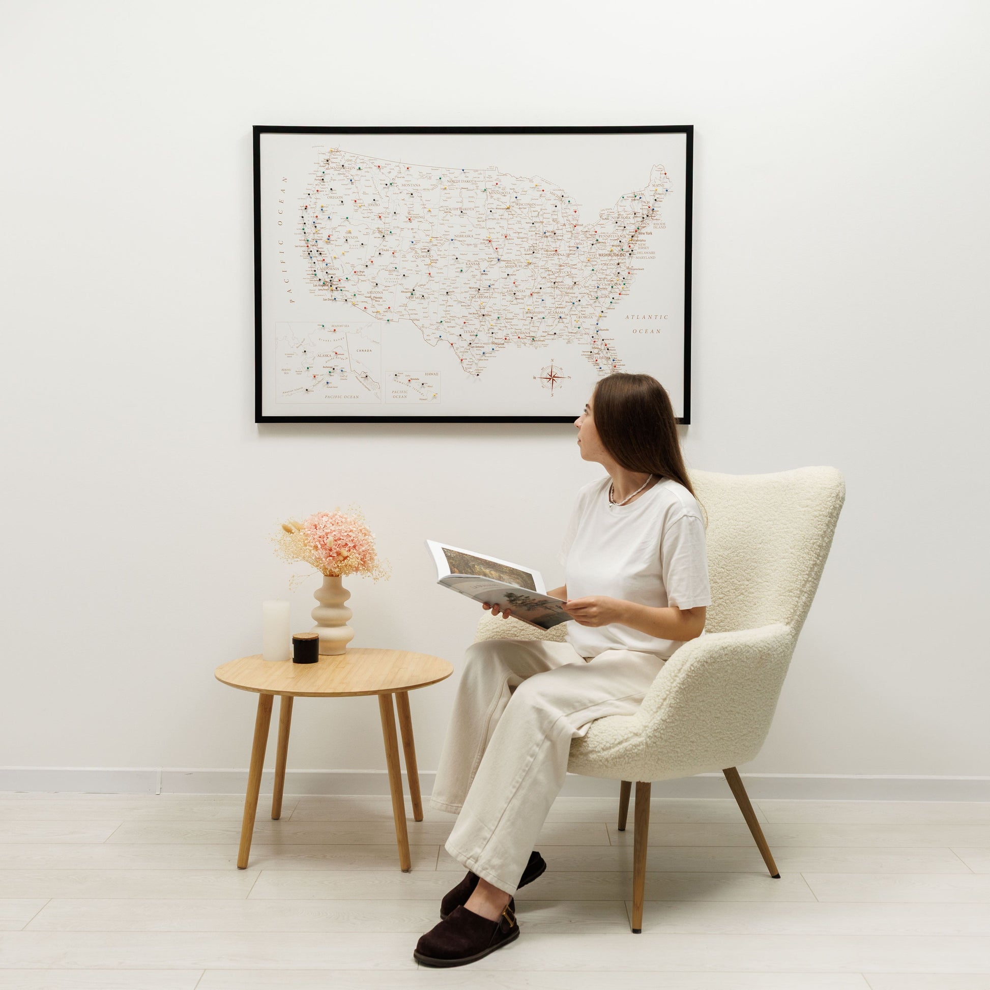 Woman sitting in a chair reading a book in a room with a framed world map on the wall.