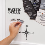 Hand placing a Hawaii magnet on a map with a compass and labeled oceans.