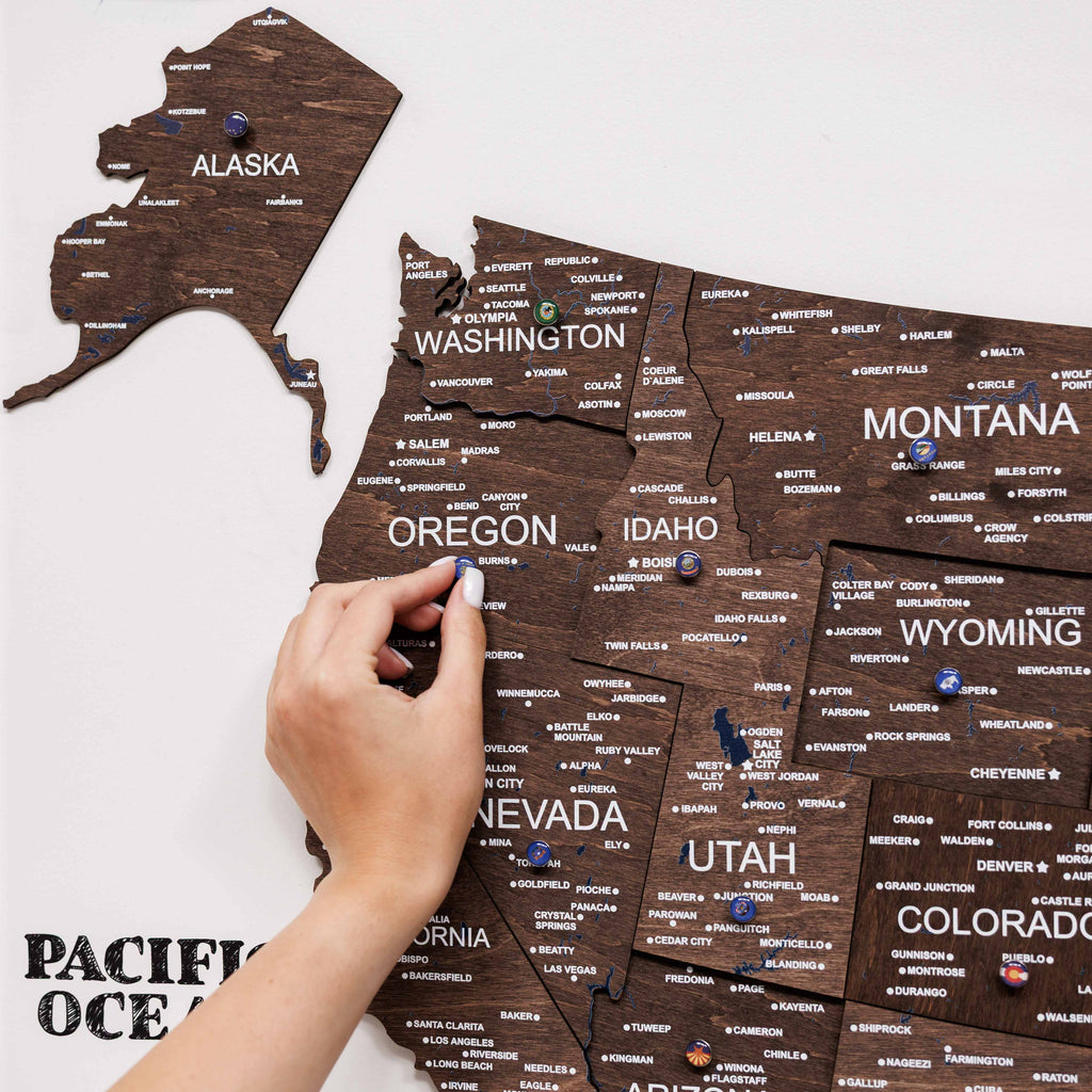 Wooden map of the United States with pins marking locations, held by a hand.