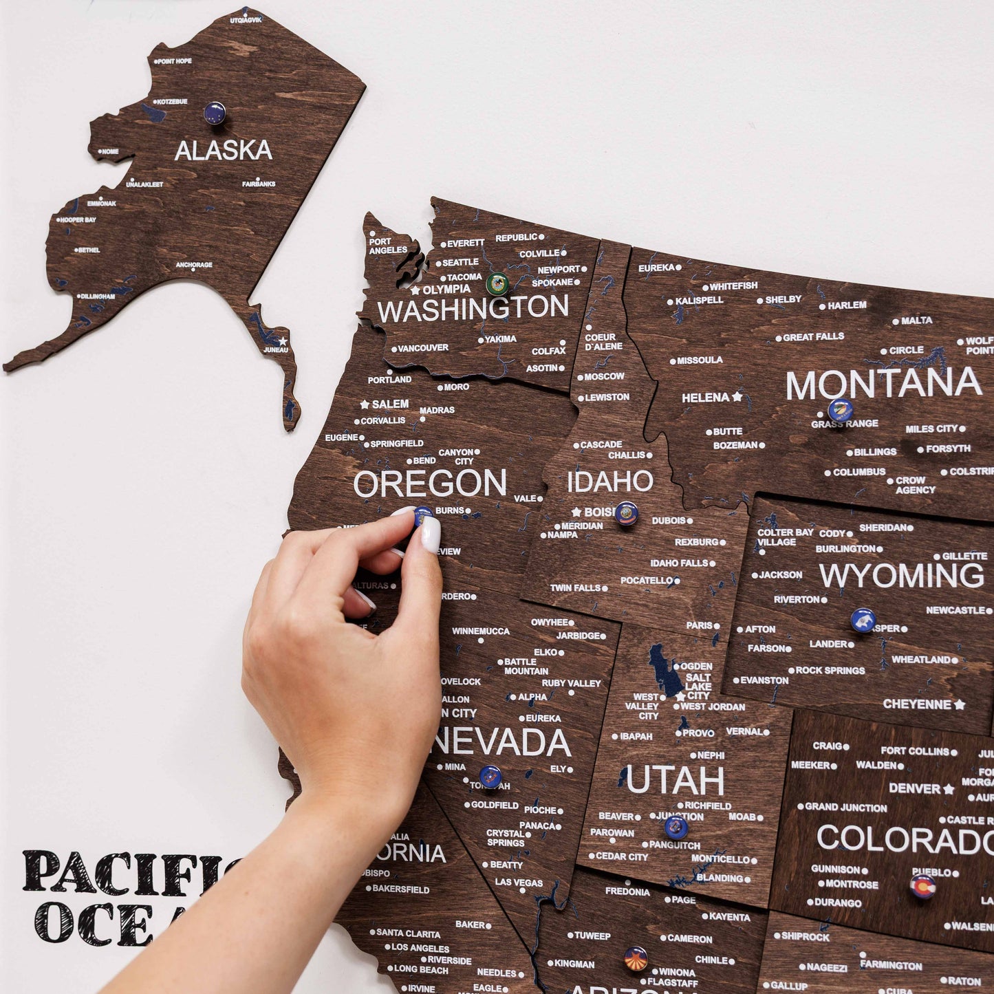 Wooden map of the United States with pins marking locations, held by a hand.