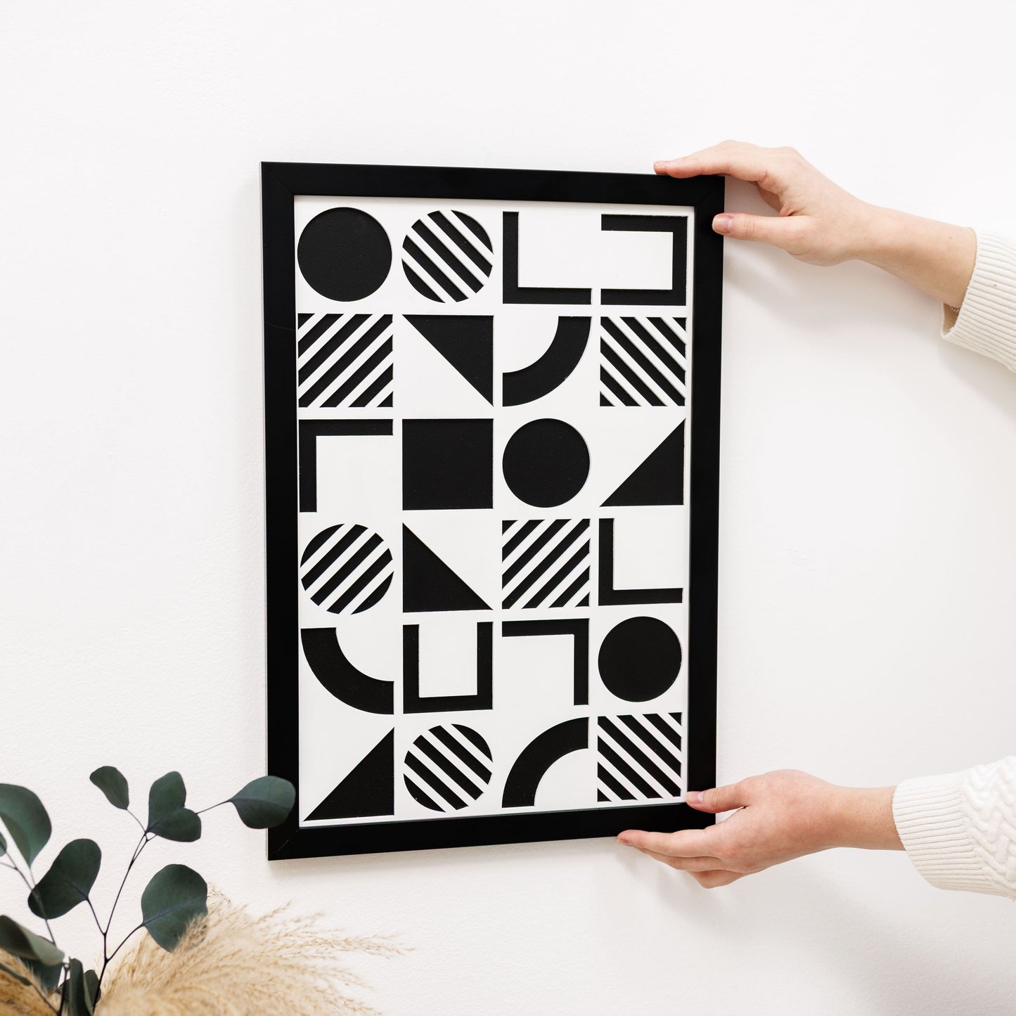 Person holding a framed black and white geometric art print on a light surface.