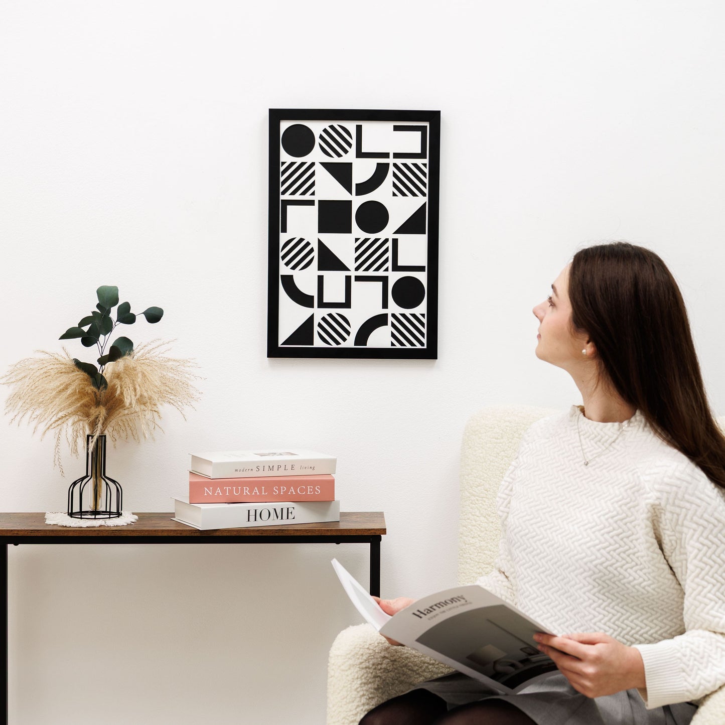 Woman reading a book in a living room with geometric art on the wall.