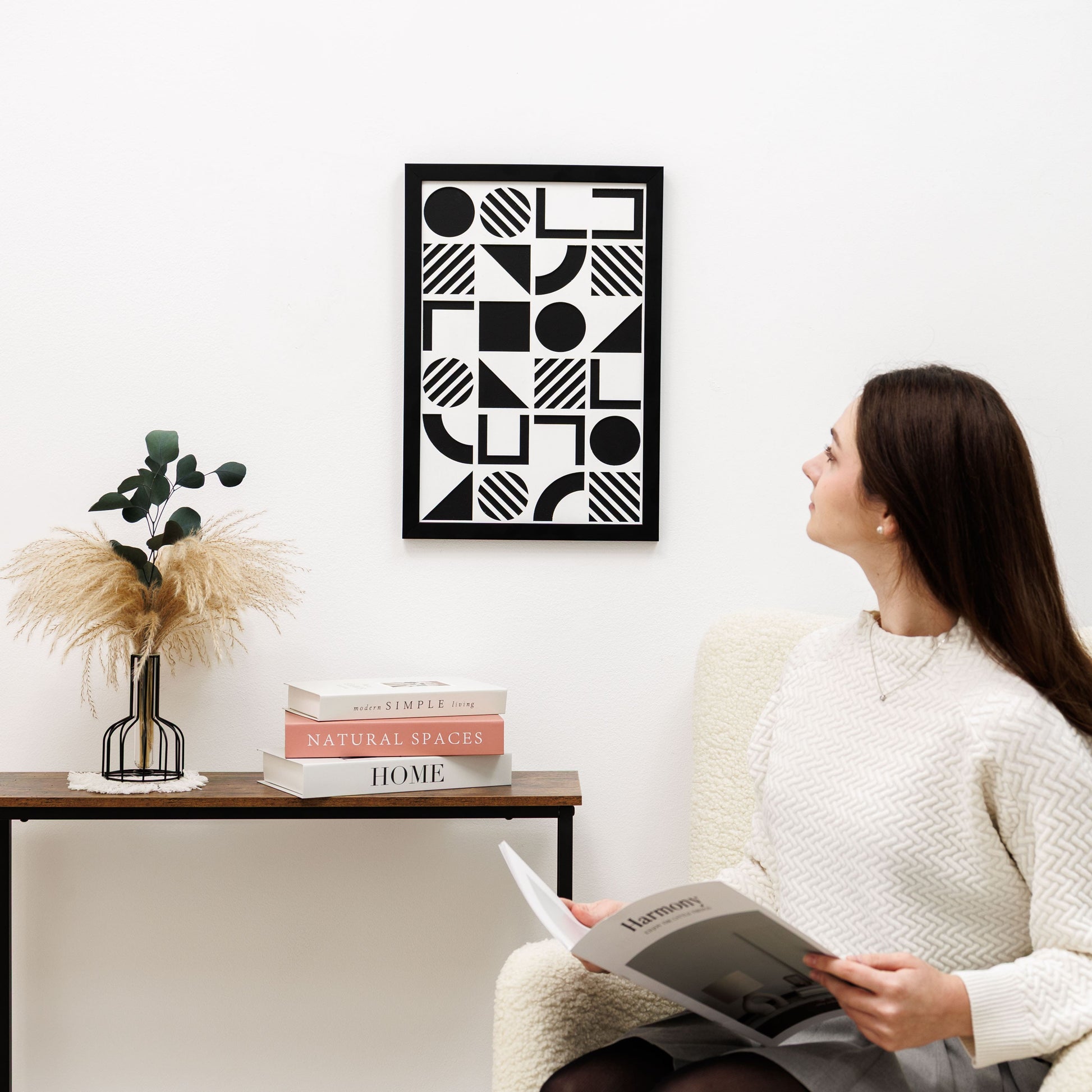 Woman reading a book in a living room with geometric art on the wall.
