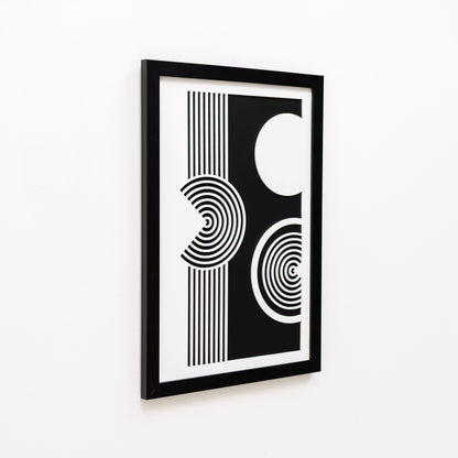 Person holding a black-framed abstract art print on a white surface with decorative elements.