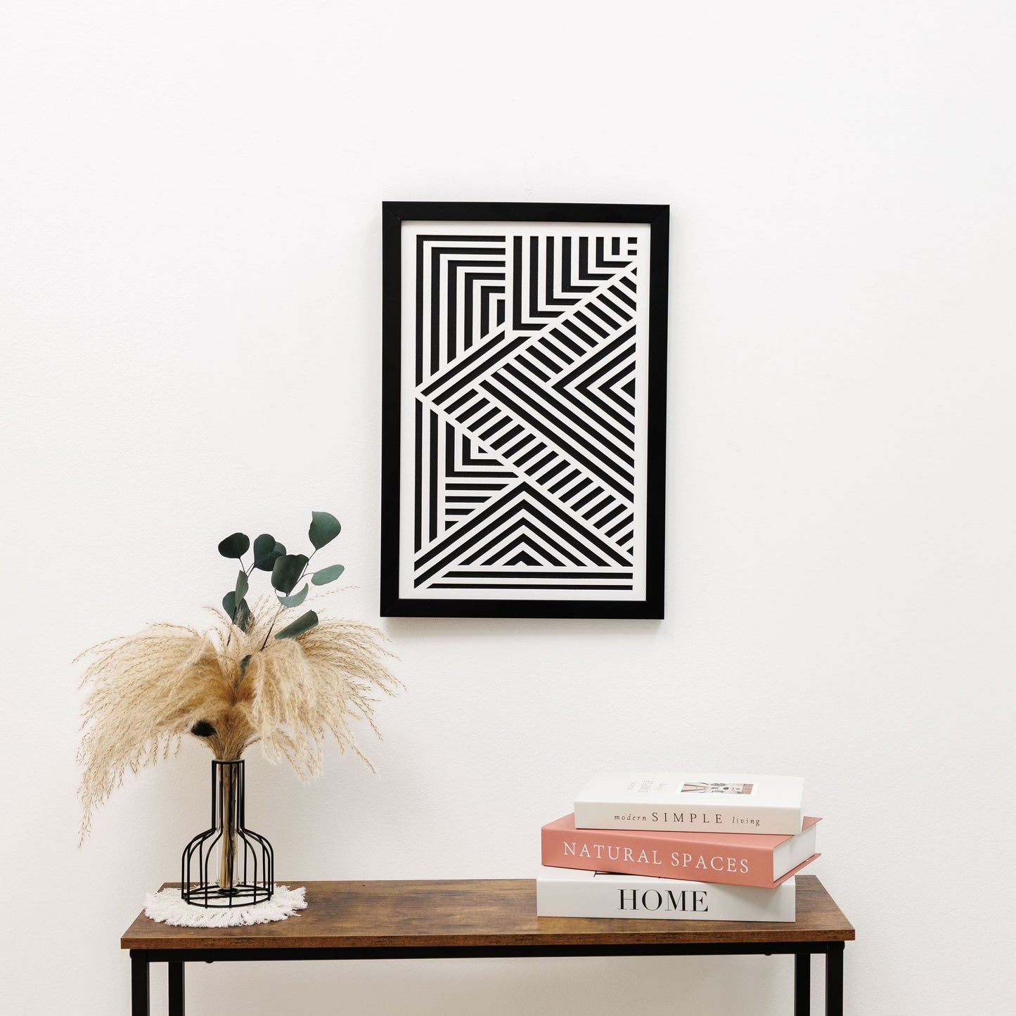 Framed geometric art piece on a wall above a wooden console table with decor items.