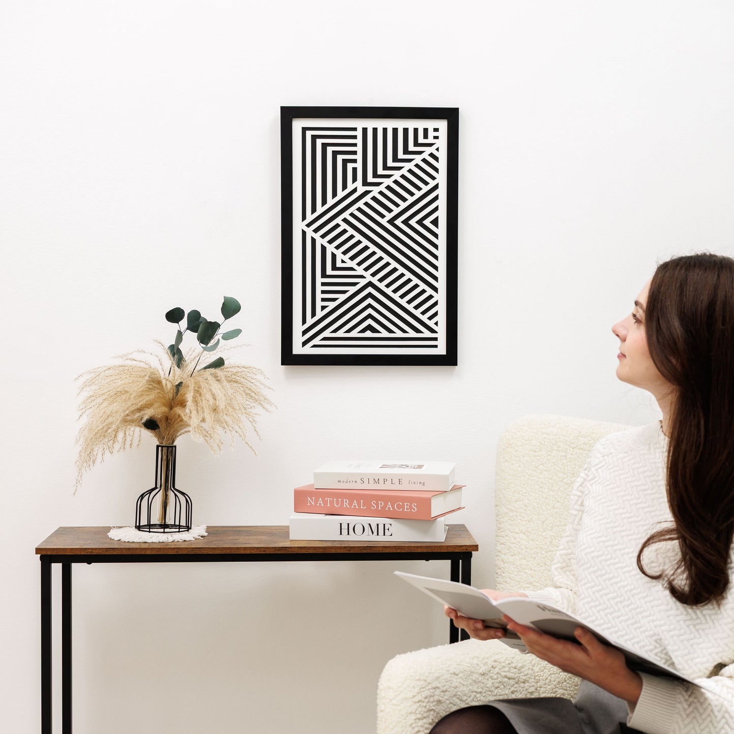 Woman sitting on a couch reading a book with a geometric art piece on the wall.