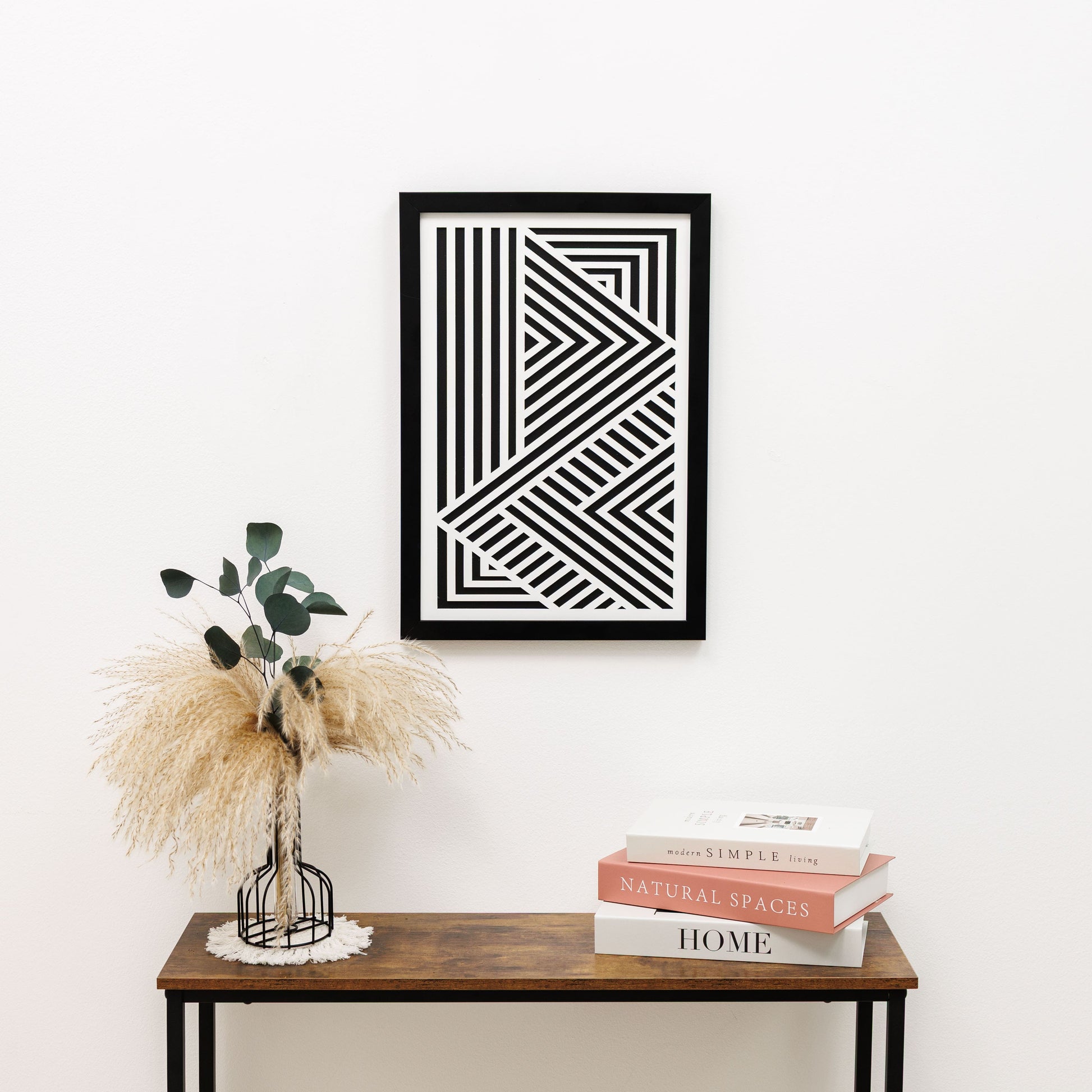 Framed geometric art piece on a wall above a wooden table with decorative items.