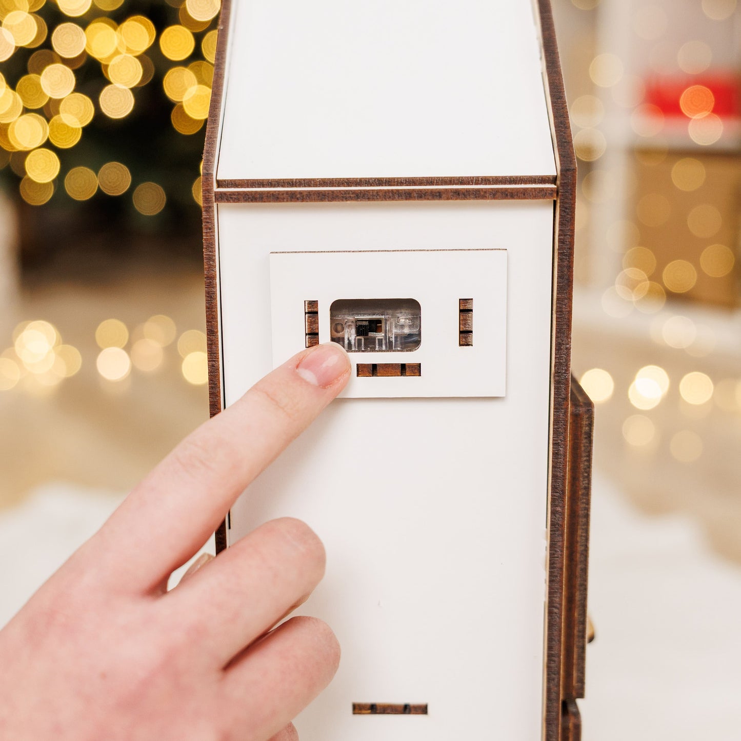 Hand pressing a button on a white electronic device with a blurred festive background