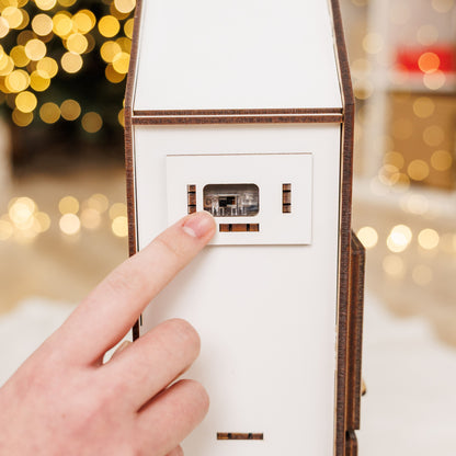 Hand pressing a button on a white electronic device with a blurred festive background