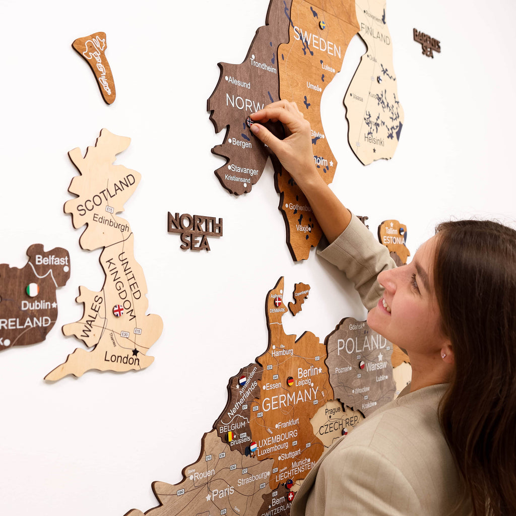 Woman arranging wooden maps of different countries on a white wall