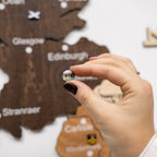 Hand holding a small round object in front of a wooden map of Scotland.
